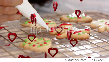 Decorating woman in light cuff applying red icing with white pastry bag on cooling-rack in kitchen Decorating woman in light cuff applying red icing with white pastry bag on cooling-rack in kitchen 141552298