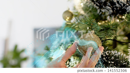 Placing hands arranging glittery gold ornament on faux green tree at home with blue particle light Placing hands arranging glittery gold ornament on faux green tree at home with blue particle light 141552306