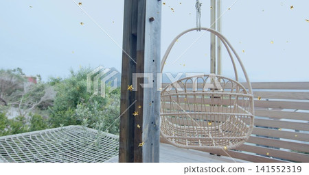 Swaying woven rattan egg chair hanging from overhead beam on beachfront deck, with net hammock Swaying woven rattan egg chair hanging from overhead beam on beachfront deck, with net hammock 141552319