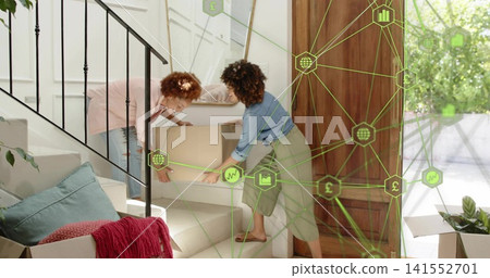 Moving two women in socks carrying moving box up carpeted stairs at home, with green overlay Moving two women in socks carrying moving box up carpeted stairs at home, with green overlay 141552701