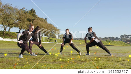 Stretching four women in black-and-white kits doing side lunges on sports field with yellow cones Stretching four women in black-and-white kits doing side lunges on sports field with yellow cones 141552727