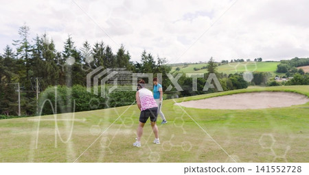 Aligning golfer in pink top putting on green while partner in teal shirt watching, with bunker Aligning golfer in pink top putting on green while partner in teal shirt watching, with bunker 141552728