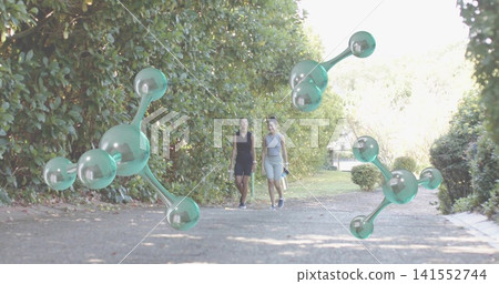 Walking two women in black-grey sleeveless outfits holding bottle along garden path with molecules Walking two women in black-grey sleeveless outfits holding bottle along garden path with molecules 141552744