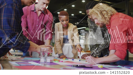 Leaning lead in beige blazer, blue top guiding five around big table with papers, charts overlaying Leaning lead in beige blazer, blue top guiding five around big table with papers, charts overlaying 141552820