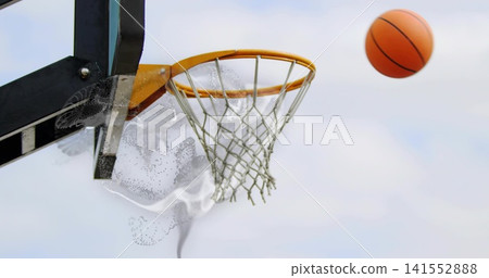 Flying basketball approaching orange rim on court by metal support, with frayed net and particles Flying basketball approaching orange rim on court by metal support, with frayed net and particles 141552888