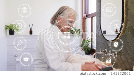 Washing senior woman wearing white terry bathrobe and eyeglasses at bathroom sink, with HUD overlay Washing senior woman wearing white terry bathrobe and eyeglasses at bathroom sink, with HUD overlay 141552961