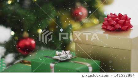 Displaying stack of wrapped gift boxes sitting on home table near decorated evergreen, with red bow Displaying stack of wrapped gift boxes sitting on home table near decorated evergreen, with red bow 141552994