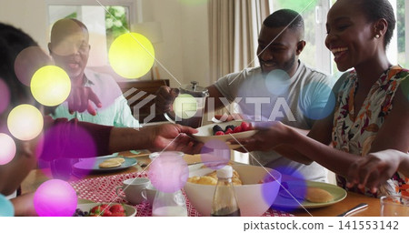Sharing family passing berry bowl and pouring French press coffee at home dining table, red runner 141553142