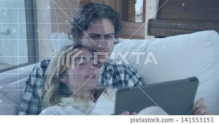 Relaxing adult females cuddling on light-colored sofa in living room, holding tablet, plaid shirt Relaxing adult females cuddling on light-colored sofa in living room, holding tablet, plaid shirt 141553151