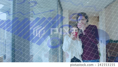Sipping red mugs, two women standing right by glass door with blue financial overlay, copy space 141553155