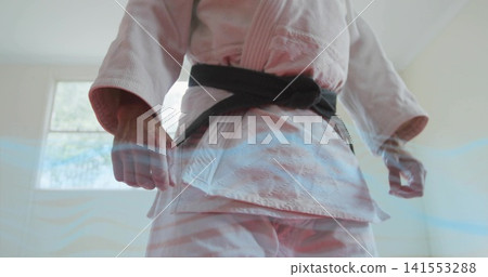 Standing martial artist in white gi and black belt clenching fists at dojo, rectangular window Standing martial artist in white gi and black belt clenching fists at dojo, rectangular window 141553288