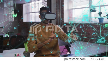 Using VR headset, man wearing brown sweater extending hands in loft, with holographic icons Using VR headset, man wearing brown sweater extending hands in loft, with holographic icons 141553303