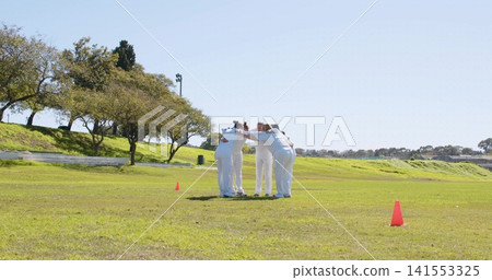 Huddling seven female players in white uniforms linking arms on grassy field, with orange cones Huddling seven female players in white uniforms linking arms on grassy field, with orange cones 141553325
