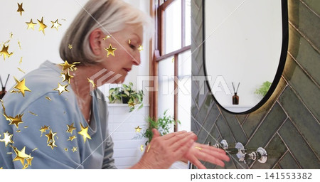 Washing hands senior woman in pale-blue top at bathroom sink, showing mirror and faucet, gold-stars Washing hands senior woman in pale-blue top at bathroom sink, showing mirror and faucet, gold-stars 141553382