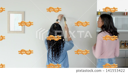 Hanging women mounting art on wall, holding hammer, in blue, pink tops, showing orange dollar signs Hanging women mounting art on wall, holding hammer, in blue, pink tops, showing orange dollar signs 141553422