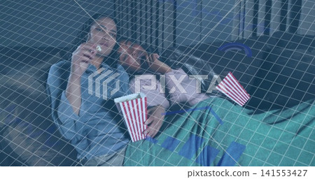 Reclining two women denim shirt, pink top on couch through mesh, holding popcorn tubs and blanket Reclining two women denim shirt, pink top on couch through mesh, holding popcorn tubs and blanket 141553427