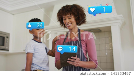 Holding tablet mom in striped apron smiling son placing hand on shoulder in kitchen showing bubbles Holding tablet mom in striped apron smiling son placing hand on shoulder in kitchen showing bubbles 141553497