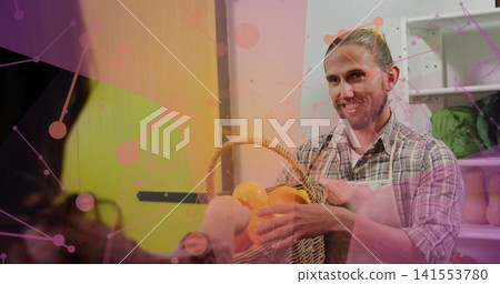 Offering bearded vendor handing woven basket of oranges behind market counter, plaid shirt apron Offering bearded vendor handing woven basket of oranges behind market counter, plaid shirt apron 141553780