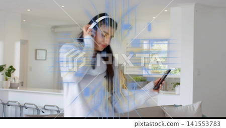 Listening woman in gray-sweater touching white headset in kitchen, holding phone with AR overlay Listening woman in gray-sweater touching white headset in kitchen, holding phone with AR overlay 141553783