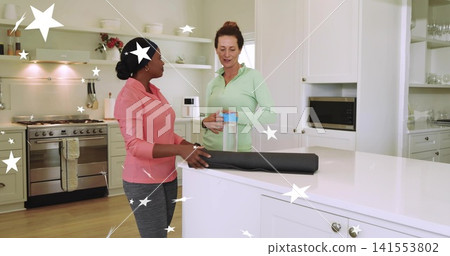 Chatting two women wearing athletic tops by kitchen island, holding blue-lid bottle, black yoga mat Chatting two women wearing athletic tops by kitchen island, holding blue-lid bottle, black yoga mat 141553802