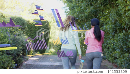 Walking 2 women in leggings, tops moving along hedged path carrying reusable bottle showing graphs Walking 2 women in leggings, tops moving along hedged path carrying reusable bottle showing graphs 141553809