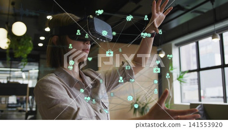 Gesturing woman wearing beige shirt manipulating holographic icons in modern office with VR headset Gesturing woman wearing beige shirt manipulating holographic icons in modern office with VR headset 141553920