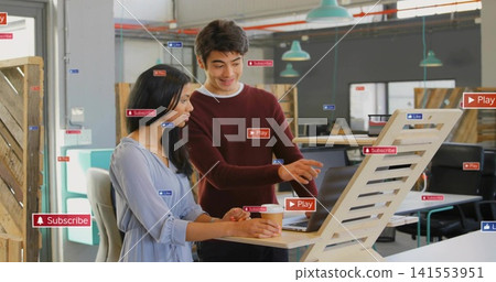 Pointing pair in maroon-top and blue-dress holding coffee-cup reviewing laptop at riser with badges Pointing pair in maroon-top and blue-dress holding coffee-cup reviewing laptop at riser with badges 141553951