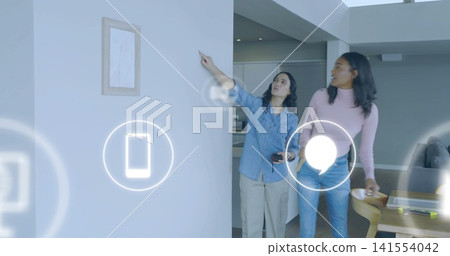 Pointing woman denim-shirt holding remote activating holographic icons on wall in home, copy space Pointing woman denim-shirt holding remote activating holographic icons on wall in home, copy space 141554042