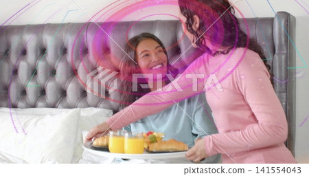 Leaning woman placing white breakfast tray on duvet at bedroom, wearing pink top, with orange juice Leaning woman placing white breakfast tray on duvet at bedroom, wearing pink top, with orange juice 141554043
