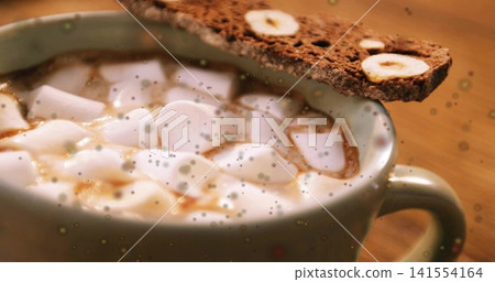 Sitting ceramic mug holding hot cocoa with soft marshmallows and biscotti on wooden table, drizzled Sitting ceramic mug holding hot cocoa with soft marshmallows and biscotti on wooden table, drizzled 141554164