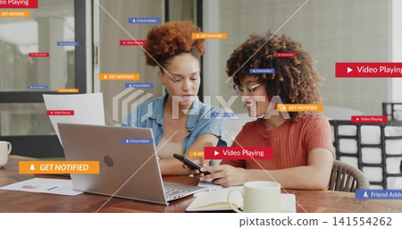 Working two women reviewing papers at office, denim shirt, rust top, laptop phone overlay labels Working two women reviewing papers at office, denim shirt, rust top, laptop phone overlay labels 141554262