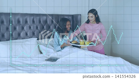 Serving woman in pink pajama pants holding breakfast tray in bed, tablet and teal graph overlay Serving woman in pink pajama pants holding breakfast tray in bed, tablet and teal graph overlay 141554326