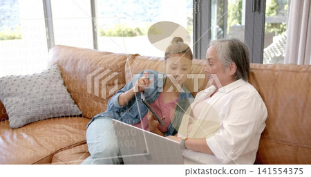 Teen tapping tablet, senior viewing laptop at home on tan leather sofa, denim jacket, overlay Teen tapping tablet, senior viewing laptop at home on tan leather sofa, denim jacket, overlay 141554375