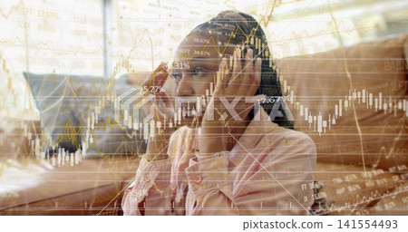 Adjusting woman in light pink shirt on tan sofa in living room, touching headphones, viewing charts Adjusting woman in light pink shirt on tan sofa in living room, touching headphones, viewing charts 141554493