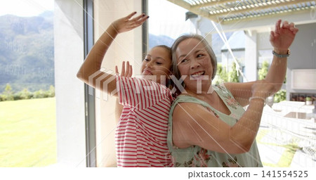 Laughing mom and daughter pressing glass door at home, wearing striped shirt, floral top, watch Laughing mom and daughter pressing glass door at home, wearing striped shirt, floral top, watch 141554525