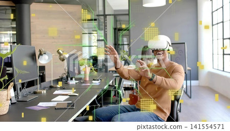 Sitting man wearing white VR headset rust sweater reaching in open office with screens, copy space 141554571