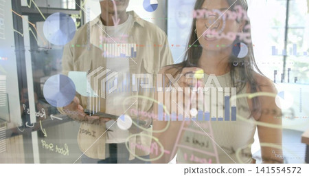 Writing woman in sleeveless top annotating glass partition at modern office, with marker and tablet Writing woman in sleeveless top annotating glass partition at modern office, with marker and tablet 141554572