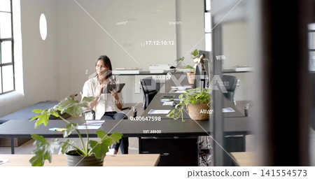 Holding tablet, Asian woman wearing light blouse, dark trousers working at black desk, copy space Holding tablet, Asian woman wearing light blouse, dark trousers working at black desk, copy space 141554573
