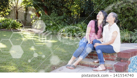 Sitting two women smiling on brick pool steps in backyard, wearing jeans and sandals, copy space Sitting two women smiling on brick pool steps in backyard, wearing jeans and sandals, copy space 141554740