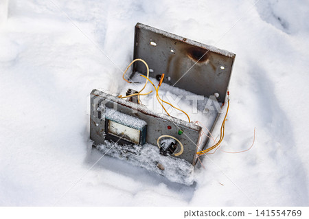 Vintage Soviet electronic device chassis dumped in deep snow, stripped for scrap metal. Industrial waste and abandonment Vintage Soviet electronic device chassis dumped in deep snow, stripped for scrap metal. Industrial waste and abandonment 141554769