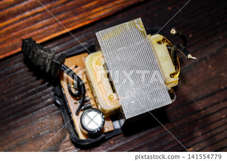 Disassembled power adapter showing the internal electrical transformer, circuit board components, and copper wiring on a dark wooden surface, capturing technical hardware repair and electronic gear Disassembled power adapter showing the internal electrical transformer, circuit board components, and copper wiring on a dark wooden surface, capturing technical hardware repair and electronic gear 141554779