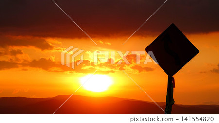 A gentle autumn evening, a slowly setting sun, and a sign silhouetted against the sky. A gentle autumn evening, a slowly setting sun, and a sign silhouetted against the sky. 141554820