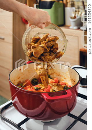 Cooking chicken with vegetables in a pot on the stove in a kitchen setting 141554890
