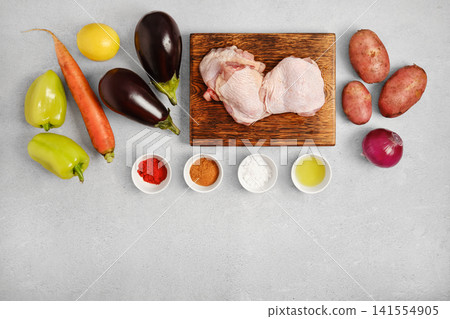 Cooking ingredients on gray surface with vegetables, chicken thighs and spices set for preparation Cooking ingredients on gray surface with vegetables, chicken thighs and spices set for preparation 141554905