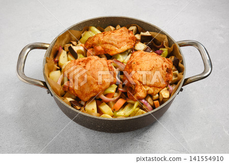 Cooking chicken thighs with vegetables in pan on kitchen counter Cooking chicken thighs with vegetables in pan on kitchen counter 141554910