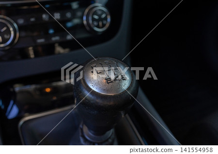 Car gear shift knob in modern vehicle interior with numbered control markings, dashboard details, steering wheel blur, dark cabin lighting, and shallow depth of field Car gear shift knob in modern vehicle interior with numbered control markings, dashboard details, steering wheel blur, dark cabin lighting, and shallow depth of field 141554958
