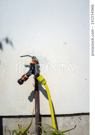 Outdoor garden water tap with orange and yellow hose connectors on weathered metal pipe against light stucco wall with utility details and connected hoses, with water, tap, garden, hose detail Outdoor garden water tap with orange and yellow hose connectors on weathered metal pipe against light stucco wall with utility details and connected hoses, with water, tap, garden, hose detail 141554966