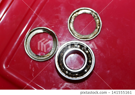 Worn out ball bearing with removed metal dust shields, showing signs of grease degradation on a vibrant red background Worn out ball bearing with removed metal dust shields, showing signs of grease degradation on a vibrant red background 141555161