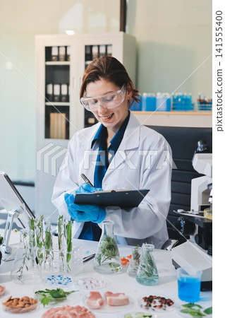Scientists in lab coats work with plants in a modern lab, focusing on research and experimentation under bright, sterile conditions. Scientists in lab coats work with plants in a modern lab, focusing on research and experimentation under bright, sterile conditions. 141555400