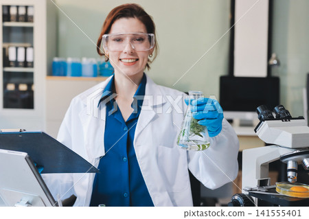 Scientists in lab coats work with plants in a modern lab, focusing on research and experimentation under bright, sterile conditions. Scientists in lab coats work with plants in a modern lab, focusing on research and experimentation under bright, sterile conditions. 141555401